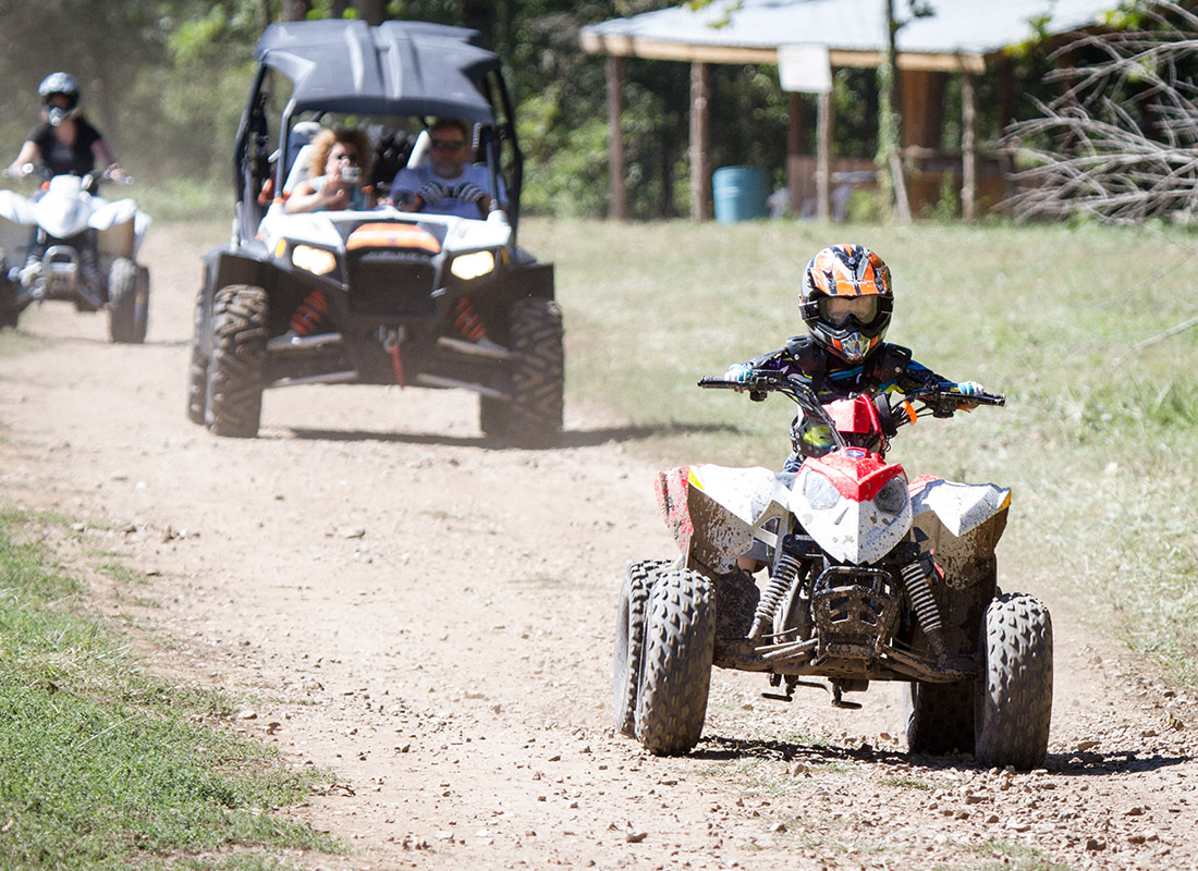 Personal Insurance - Young Child Riding a ATV With Parents Riding and Watching from Behind on a Sunny Day